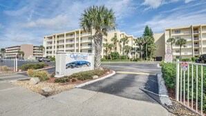 A gated entrance to Castleberry Condominiums with a sign, palm trees, and a clear sky. - New Smyrna Beach Condo w/ Ocean-view Balcony! (New Smyrna Beach)