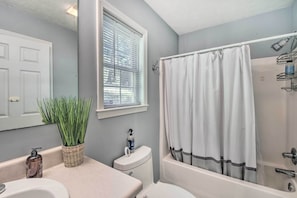 A bathroom with a bathtub, toilet, sink, and a window with blinds.