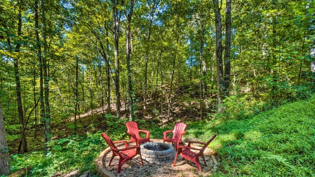 Un espace circulaire aménagé avec des sièges autour d’un foyer, le tout entouré de quatre chaises rouges, dans un cadre forestier.