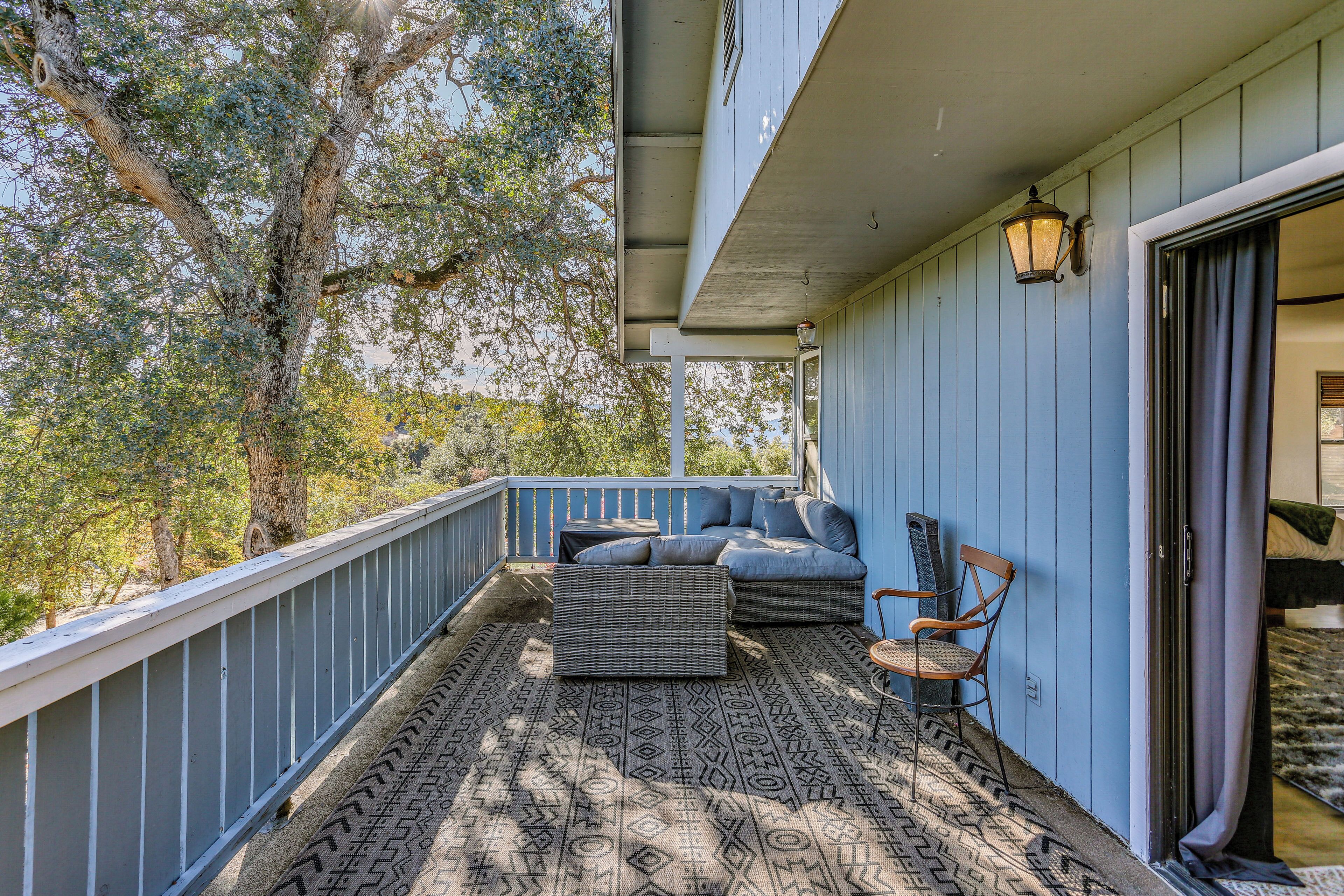 A balcony with wicker furniture, a patterned rug, and a view of trees.