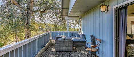 A balcony with wicker furniture, a patterned rug, and a view of trees.