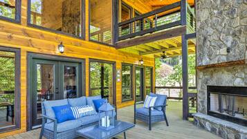 A wooden deck with outdoor furniture, a stone fireplace, and large windows.