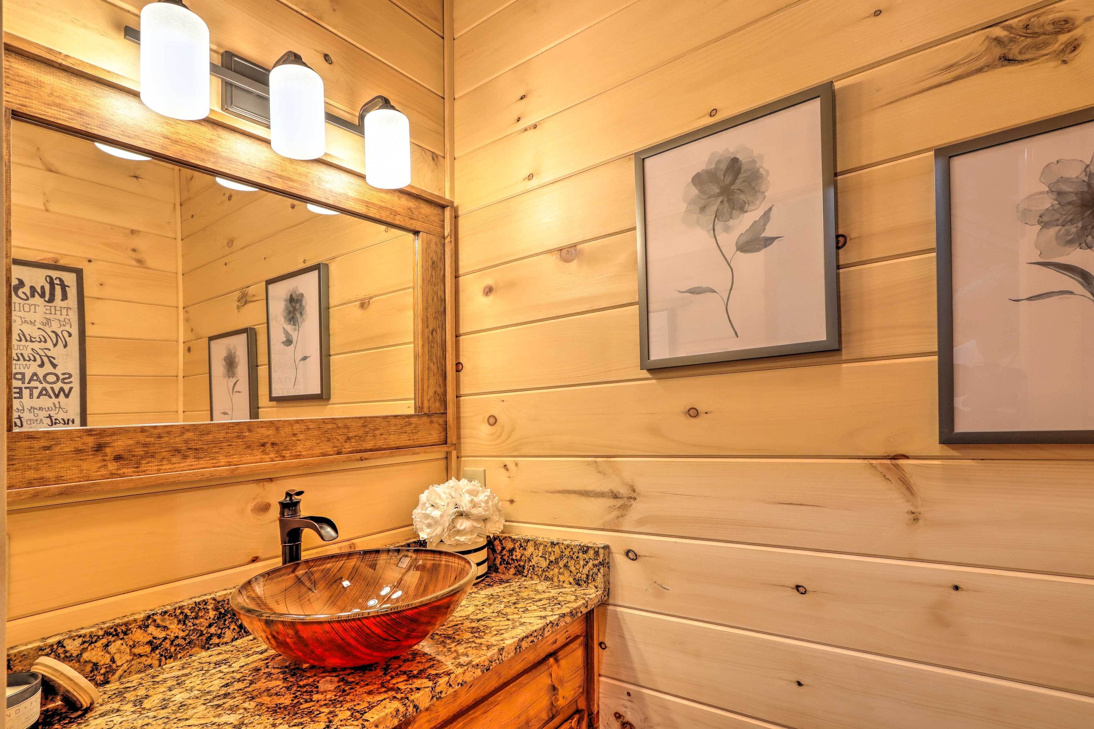 A wooden cabin bathroom with a granite countertop, a glass bowl sink, and framed floral artwork on the walls.