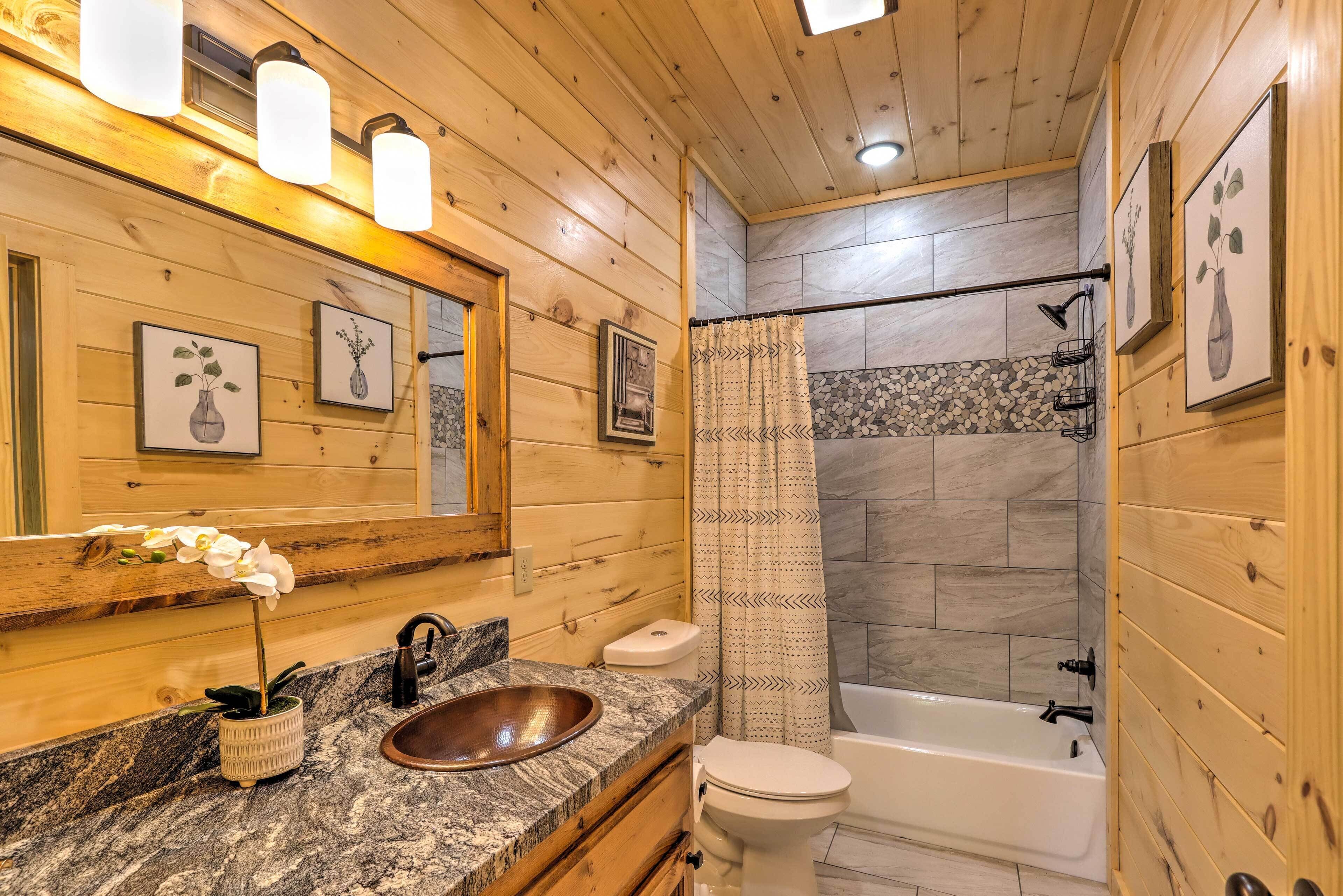 Une salle de bain rustique, avec des murs en bois, un comptoir en granit, un lavabo sur pied, des toilettes et une baignoire.