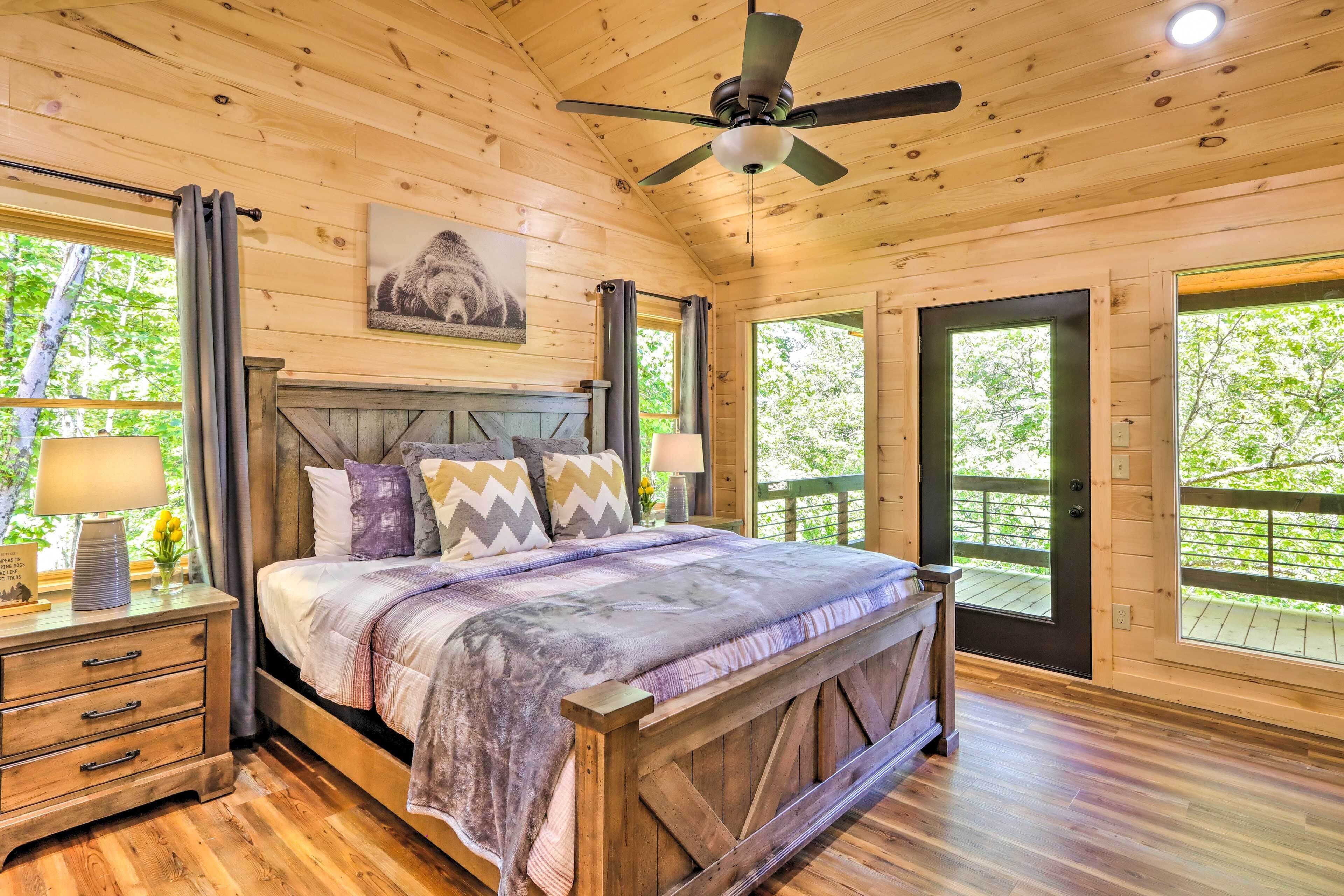 A wooden cabin bedroom with a bed, nightstands, a ceiling fan, and large windows.