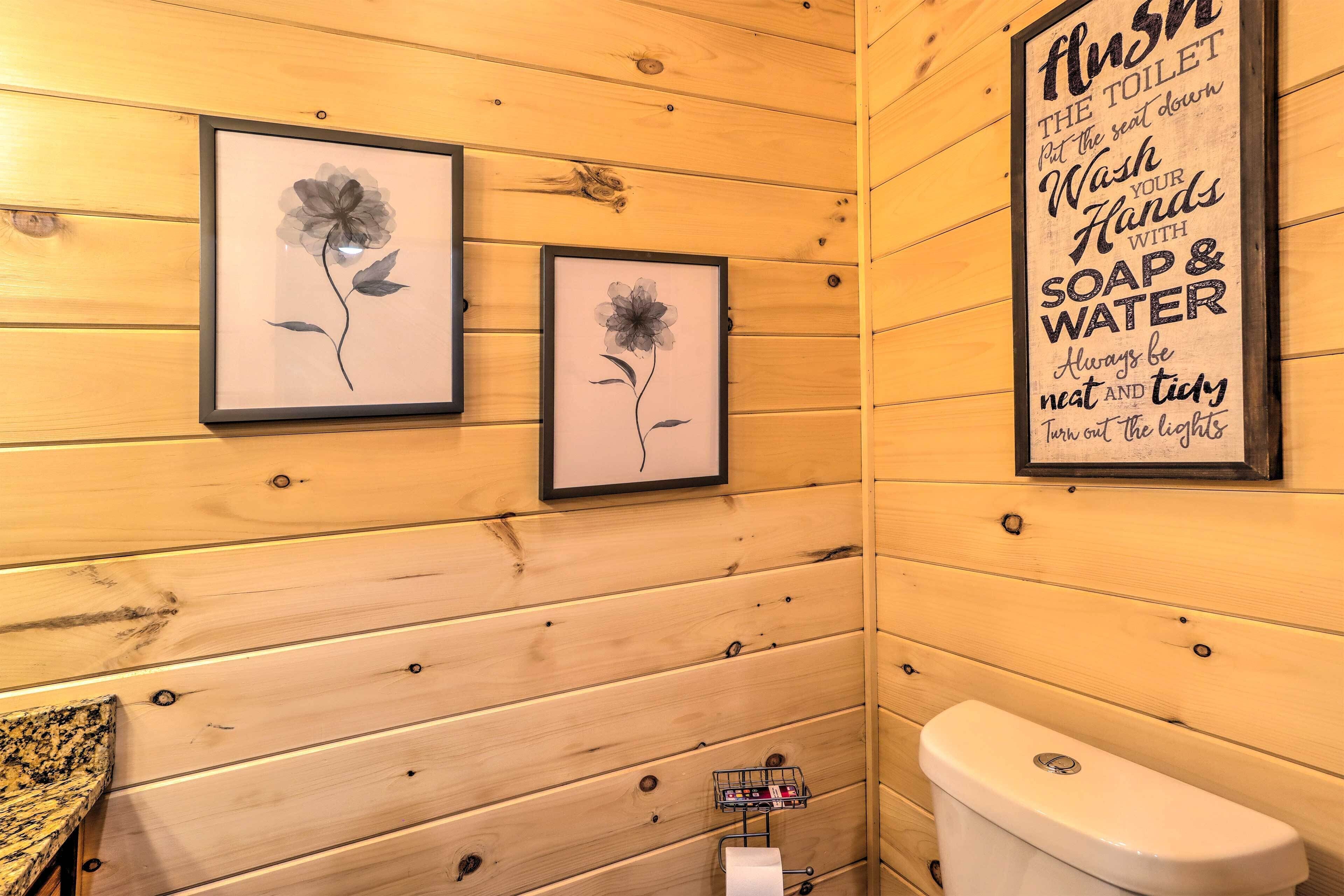 A wooden bathroom with framed floral artwork, a toilet, and a sink with a soap dispenser.