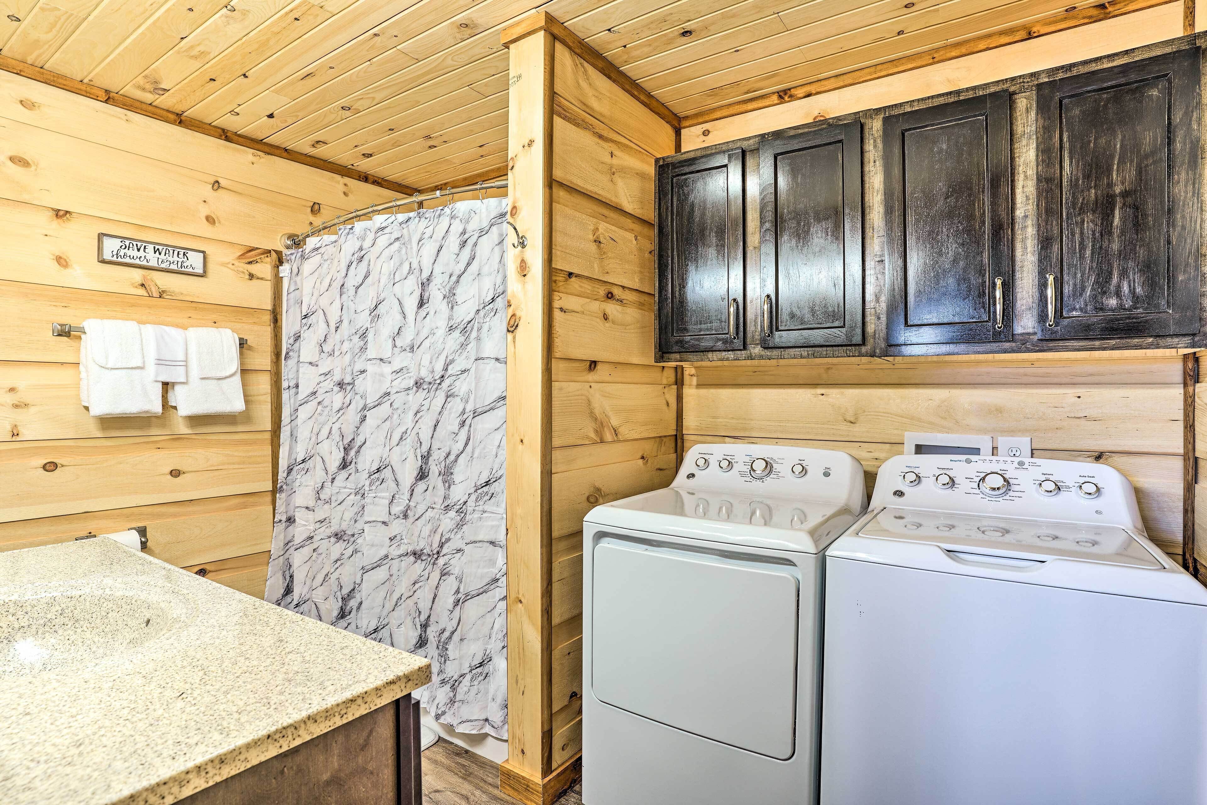Un espace intérieur compact, aménagé en bois, comprenant un lave-linge et un sèche-linge, un porte-serviettes et un panneau encourageant à économiser l’eau.