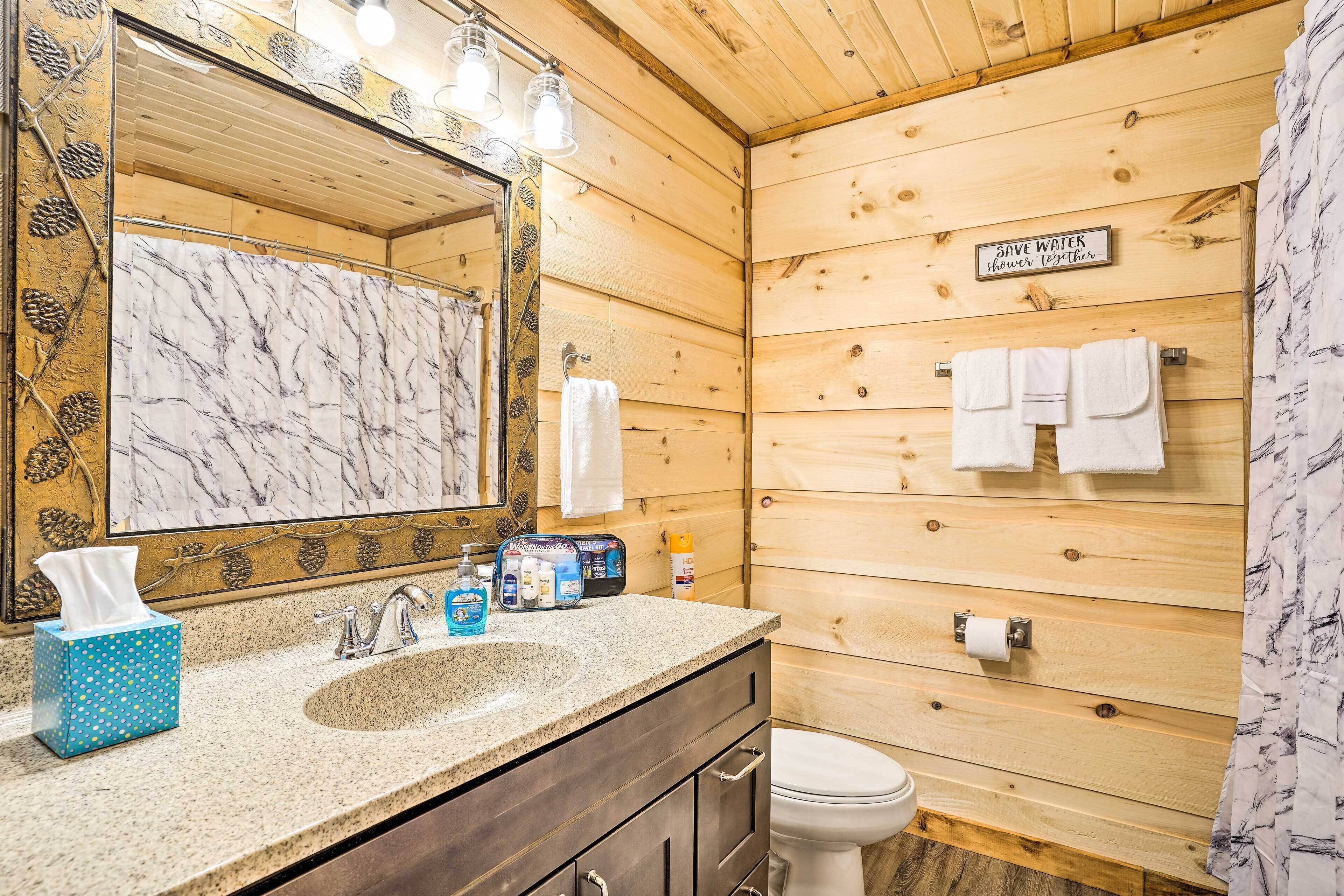 Un baño con interior de madera, lavamanos con azulejos de mármol, espejo con iluminación y un cartel que promueve el ahorro de agua.