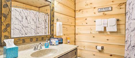 Un baño con interior de madera, lavamanos con azulejos de mármol, espejo con iluminación y un cartel que promueve el ahorro de agua.