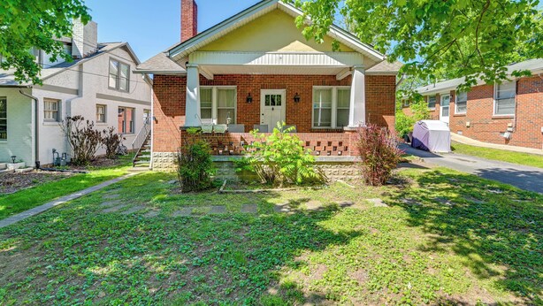 A two-story brick house with a front porch, a small front yard, and a visible chimney.