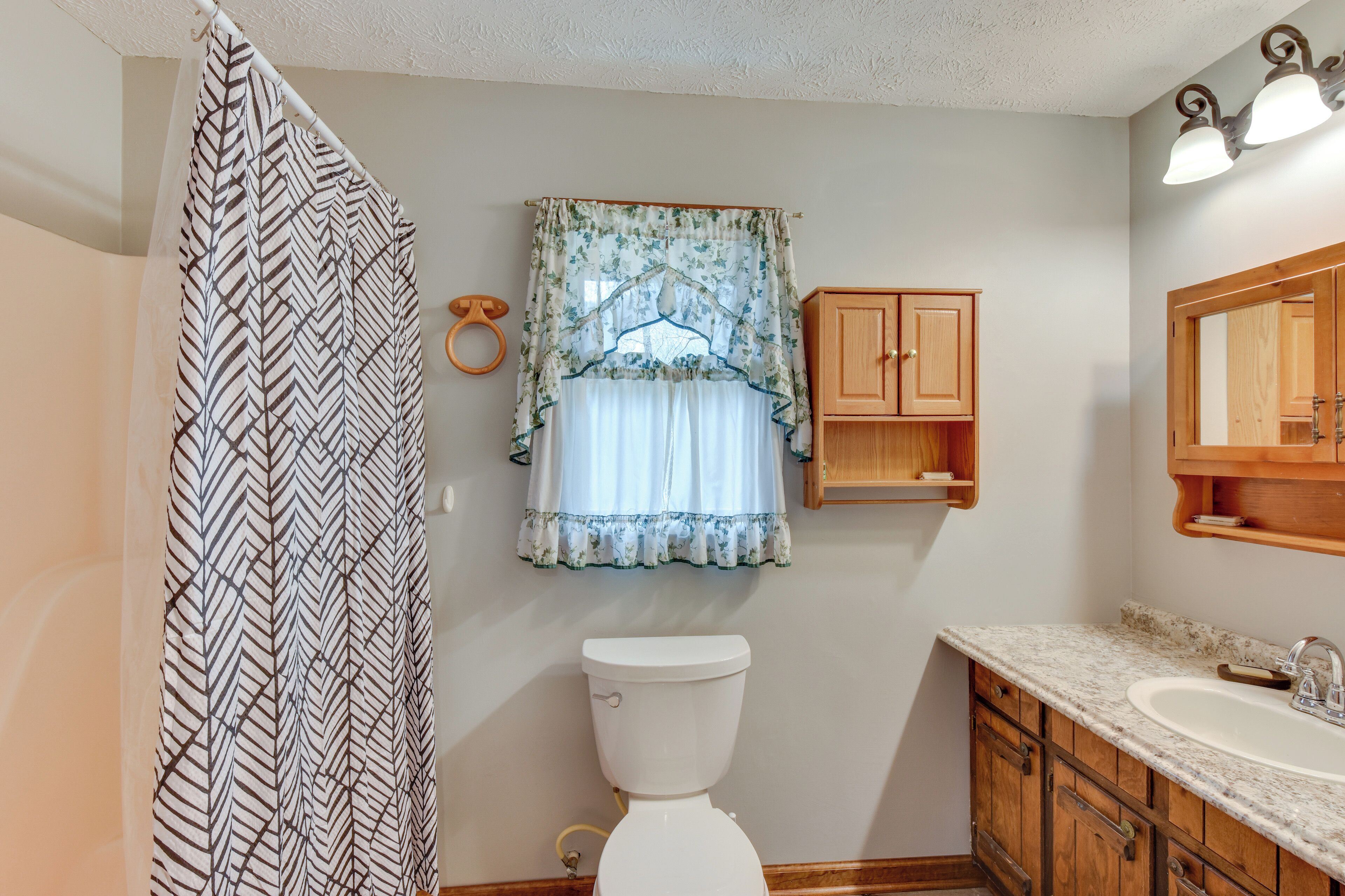 A bathroom with a toilet, wooden cabinets, a sink, and a shower curtain.