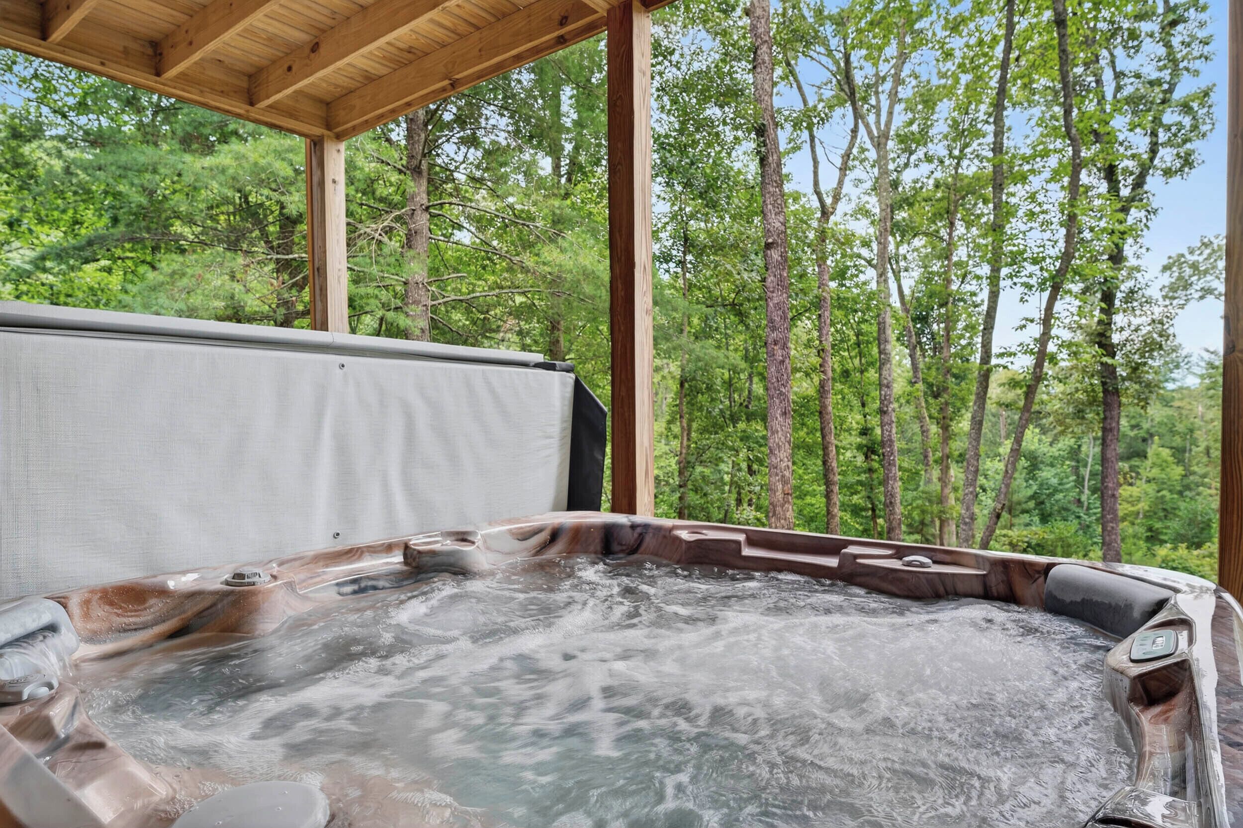 A hot tub with a wooden deck and a view of a forest.