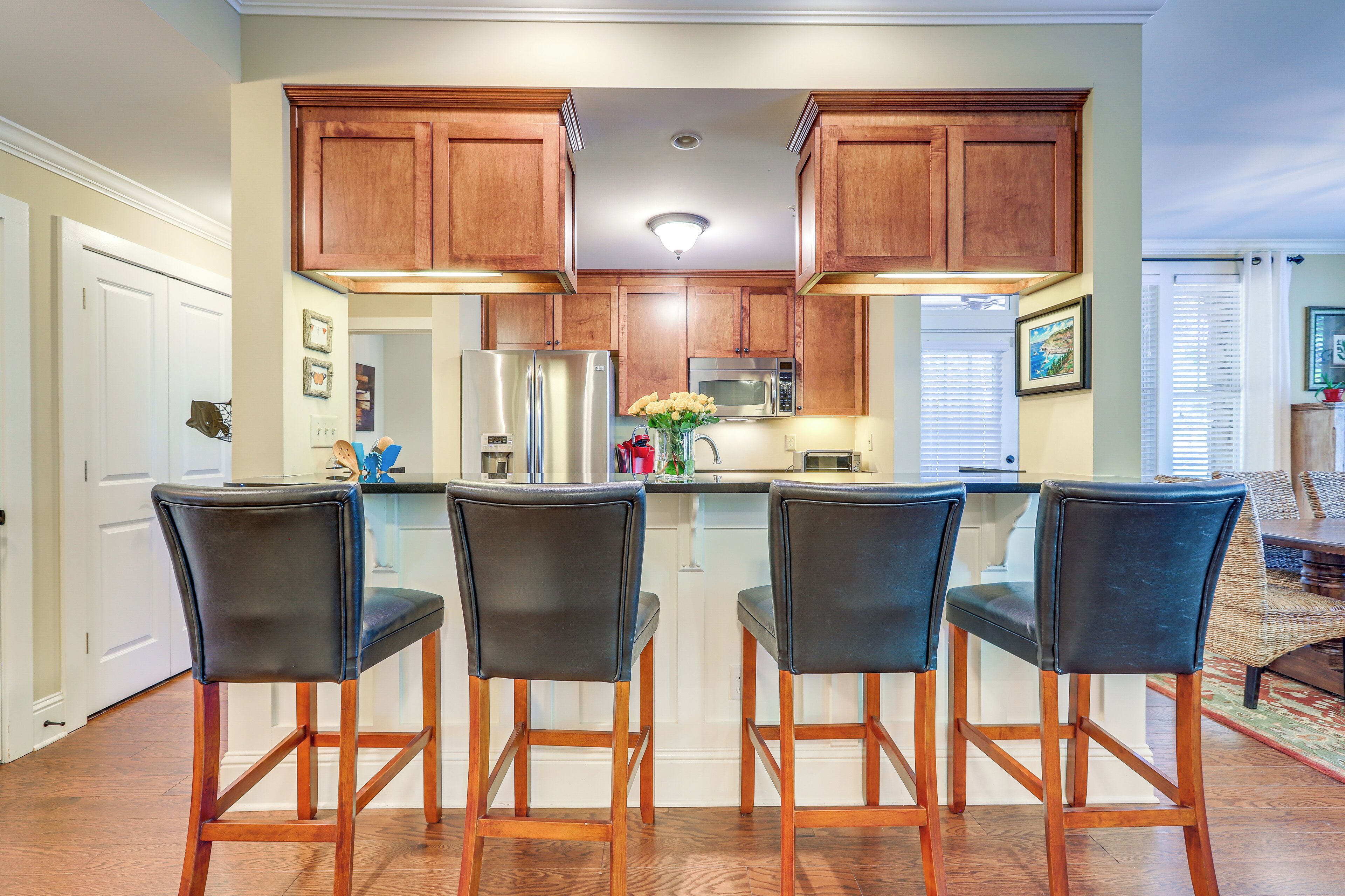 Eine Küche mit Holzausstattung, einem Edelstahlkühlschrank, einer Mikrowelle und einer Bar mit vier Sitzplätzen.