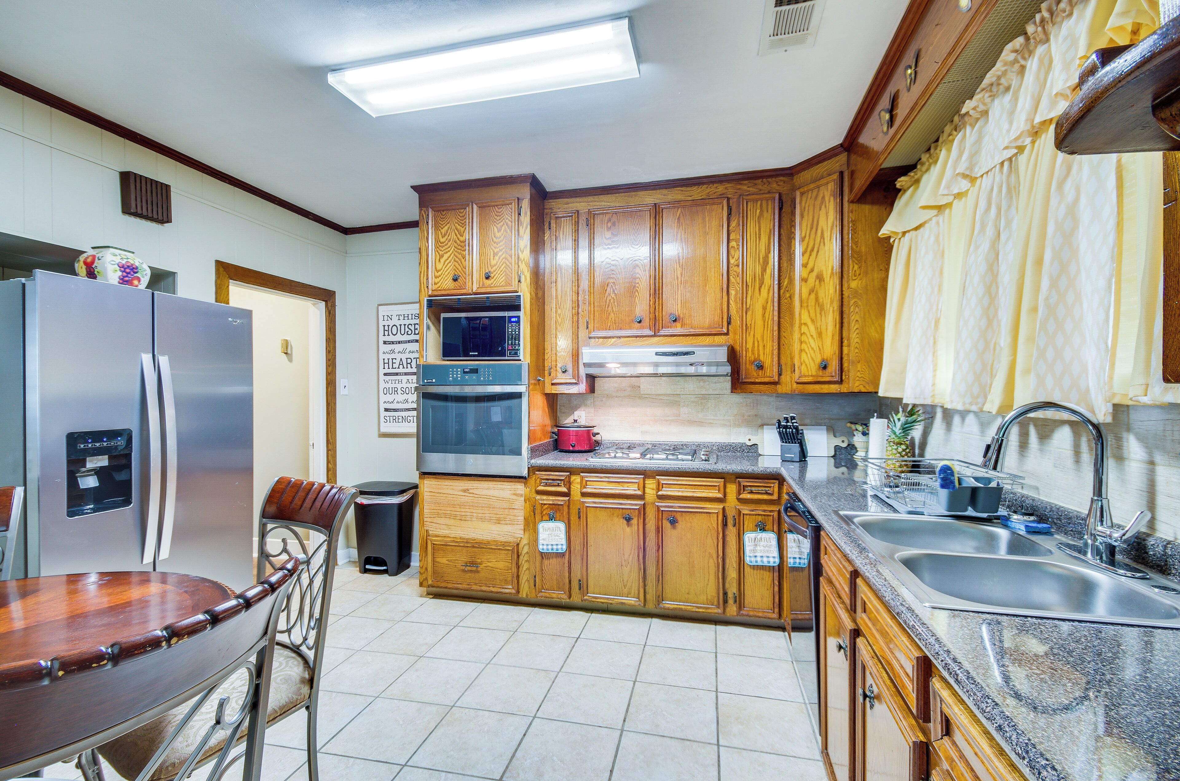 A kitchen with wooden cabinets, stainless steel appliances, a granite countertop, and a dining area with a wooden table and metal chairs.