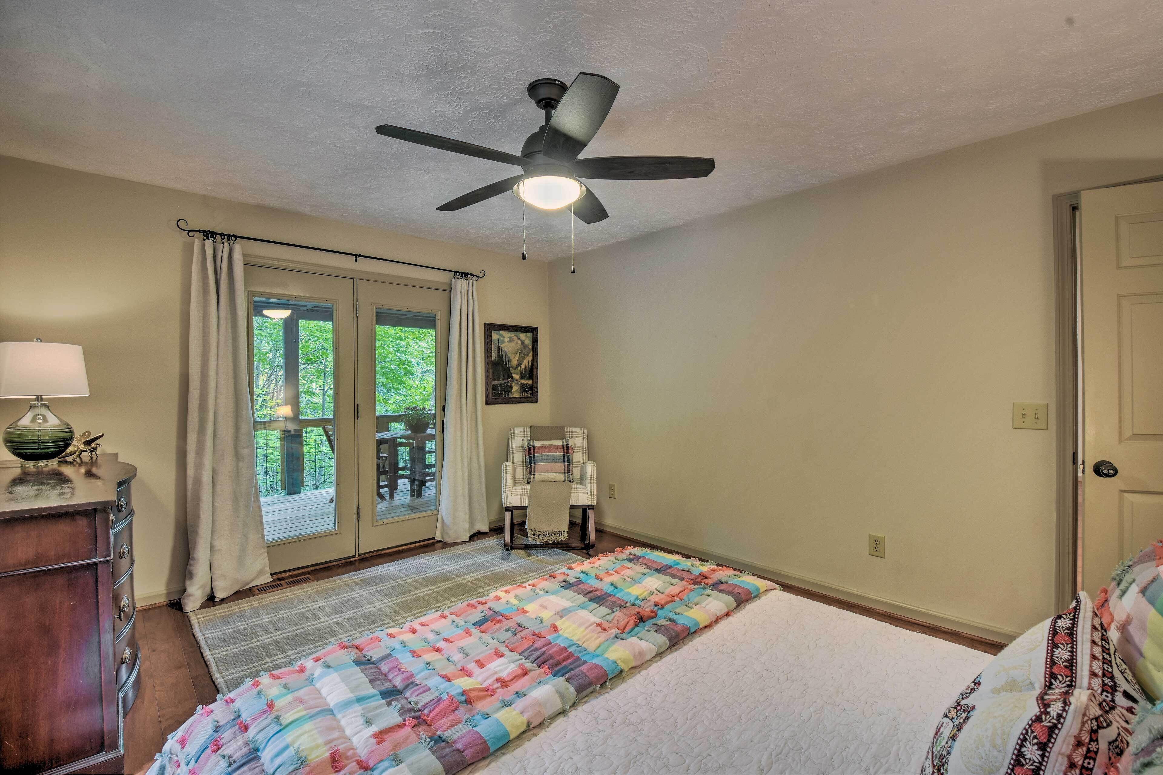 Une chambre à coucher comprenant un lit, un ventilateur de plafond, une fenêtre avec des rideaux, une chaise et une table de chevet avec une lampe.