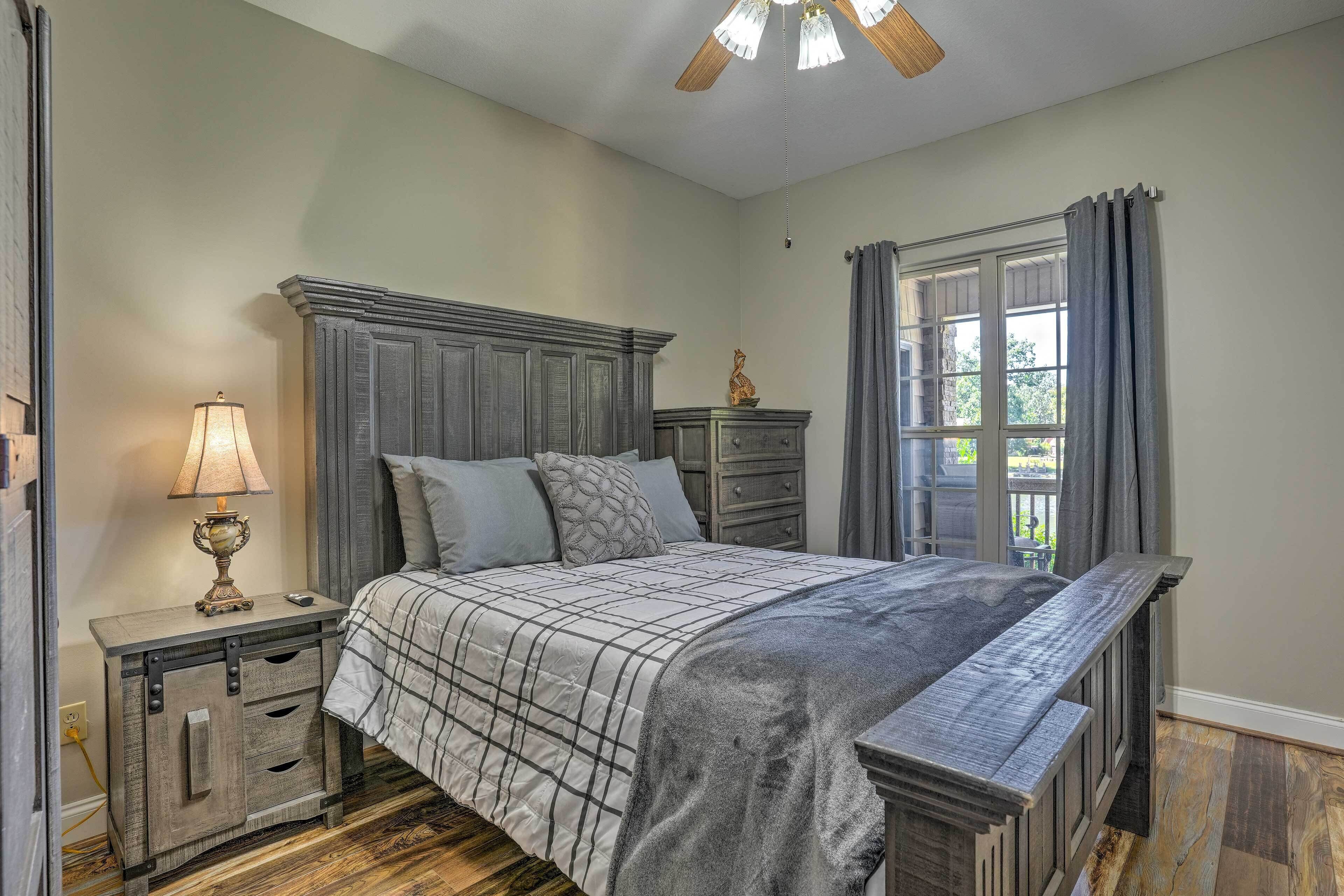 Quarto com cama, mesa de cabeceira, cômoda e janela com cortinas.