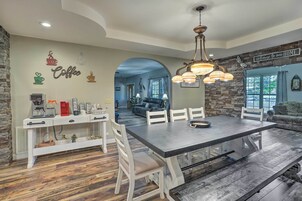 A dining area with a large table, white chairs, and a coffee station.