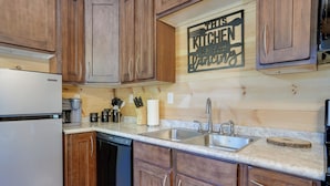 Una cocina con armarios de madera, un lavamanos de acero inoxidable y una encimera con varios utensilios de cocina.