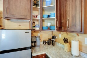 Una cocina con armarios de madera, un refrigerador blanco, una cafetera y diversos utensilios de cocina.