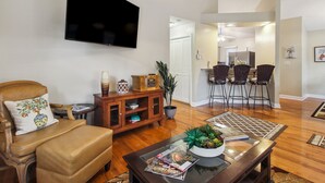 A living room with a flat-screen TV, leather armchair, coffee table with magazines, and a dining area with chairs and a table. - Savannah Home w/ Patio & Grill ~ 2 Mi to Downtown (Savannah)
