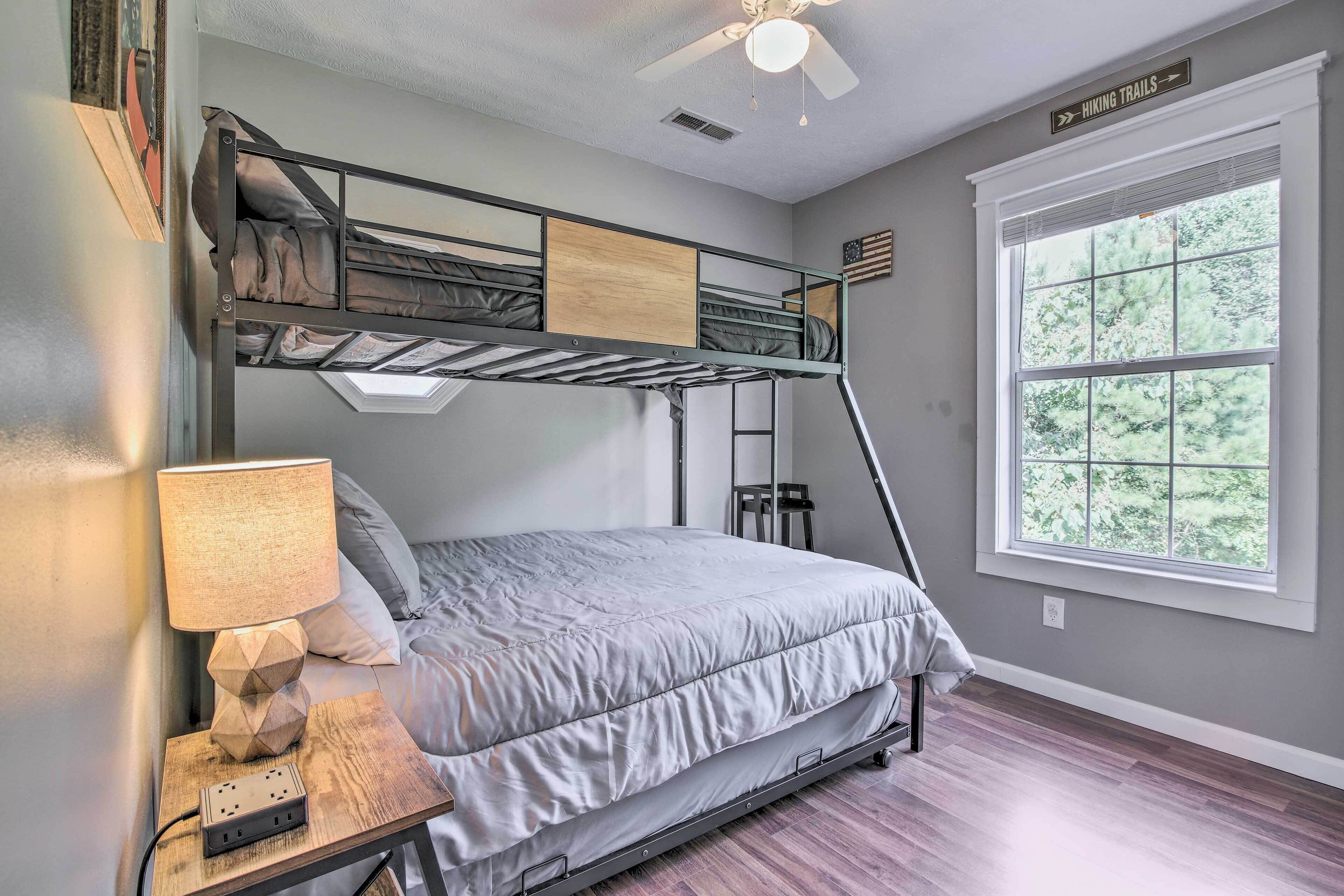 A bunk bed room with a desk, lamp, and a window with a view of trees.