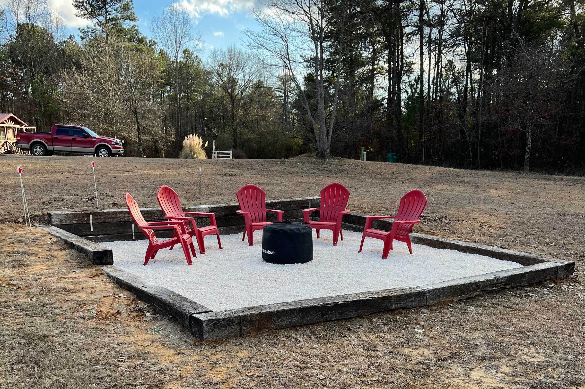 A deck with red Adirondack chairs and a black ottoman, surrounded by a wooden deck and a grassy area.