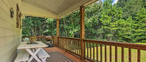 A covered porch with a wooden table and benches, overlooking a grassy area with trees.