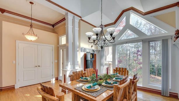 A dining area with a wooden table set for six, surrounded by wooden chairs.