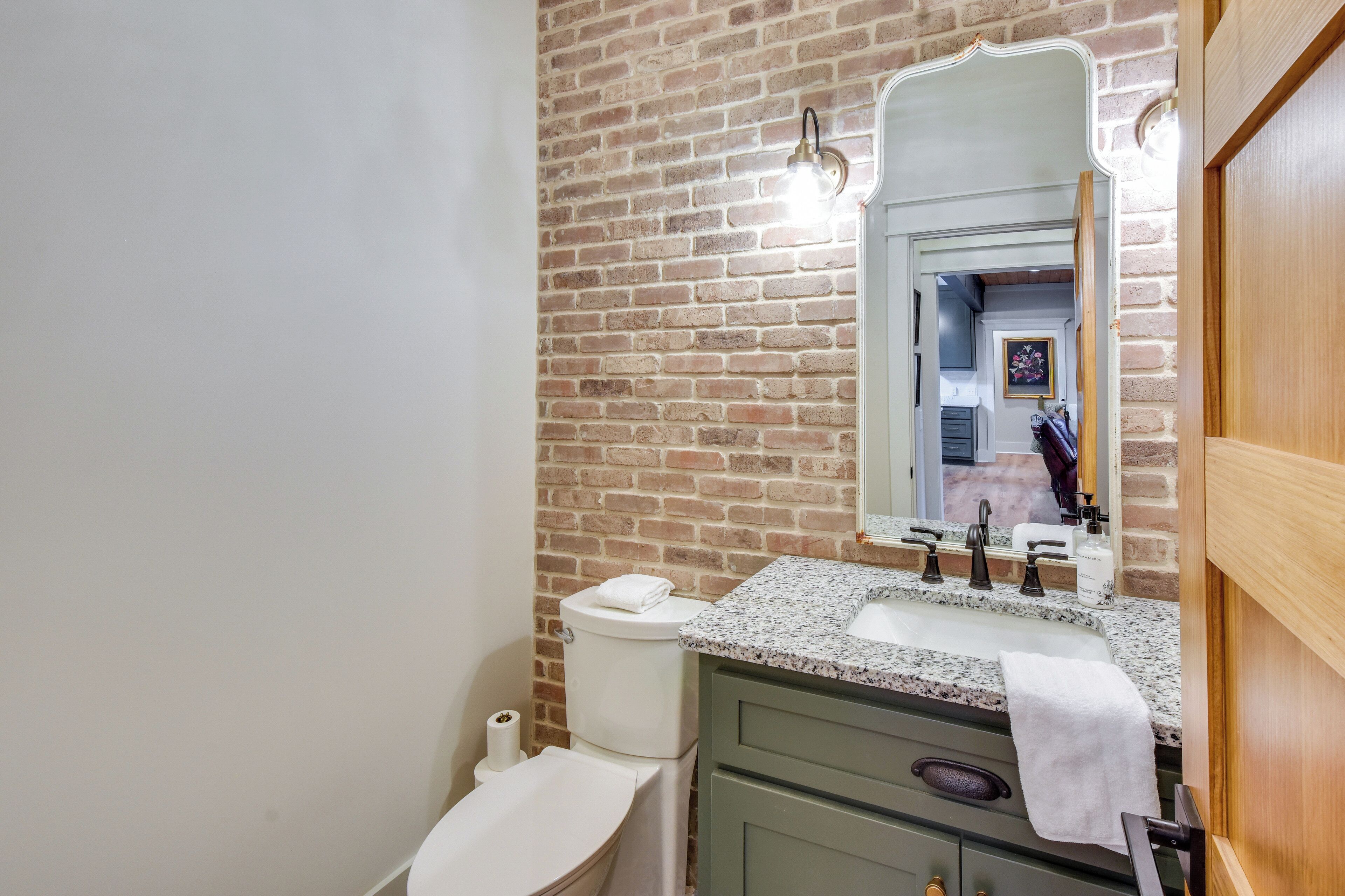 A bathroom with a brick wall, a white toilet, a sink with a mirror, and a wooden door.