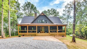 A two-story log cabin with a wrap-around porch, a chimney, and a gravel driveway. - Luxurious Clarkesville Cabin w/ Decks & Fire Pit (Clarkesville)