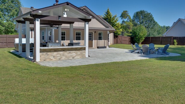 A covered patio area with a barbecue grill, outdoor seating, and a view of the backyard. - Spacious Winder Getaway w/ Hot Tub + Game Room! (Winder)