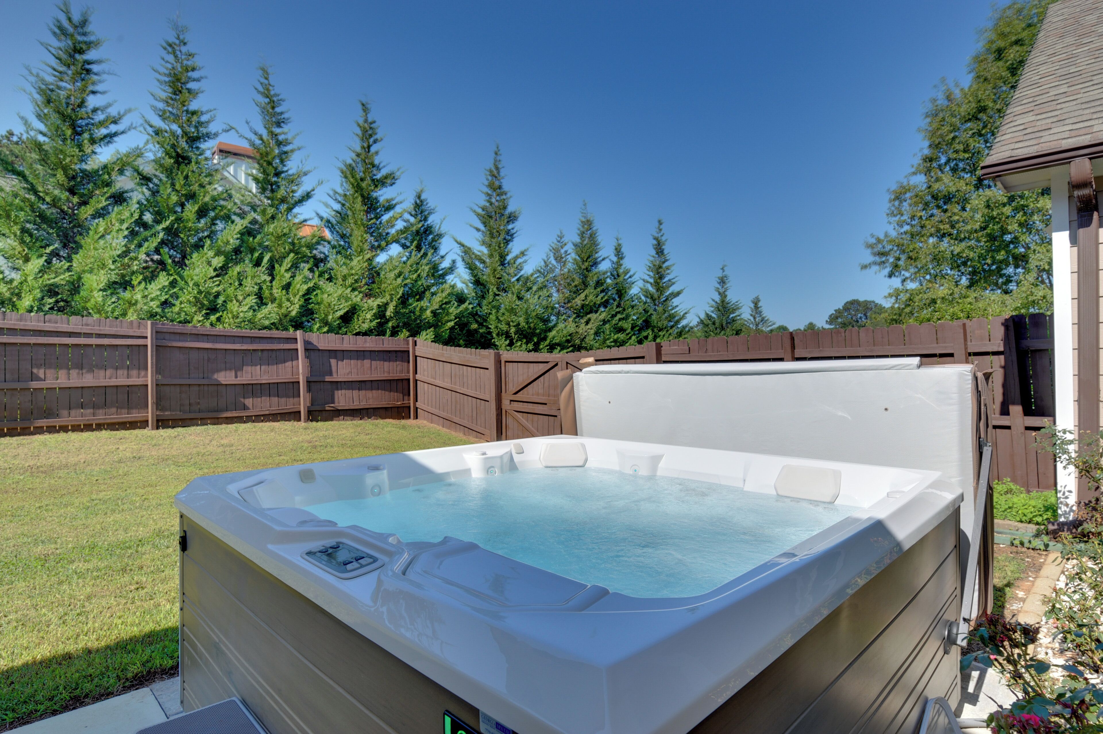 A hot tub in a backyard with a wooden fence and trees in the background.