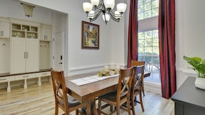 A dining area with a wooden table, chairs, a chandelier, a painting, and a window with curtains. - Spacious Winder Getaway w/ Hot Tub + Game Room! (Winder)