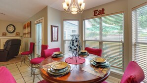 A dining area with a round table set for four, surrounded by red chairs, a chandelier, and large windows with blinds. - Horn Lake Home w/ Yard: 8 Mi to Graceland! (Horn Lake)