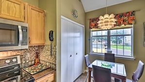 A kitchen with wooden cabinets, a microwave, a stove, and a dining area with a table and chairs. - Buckroe Beach Retreat 5 Min to the Sand (Hampton)