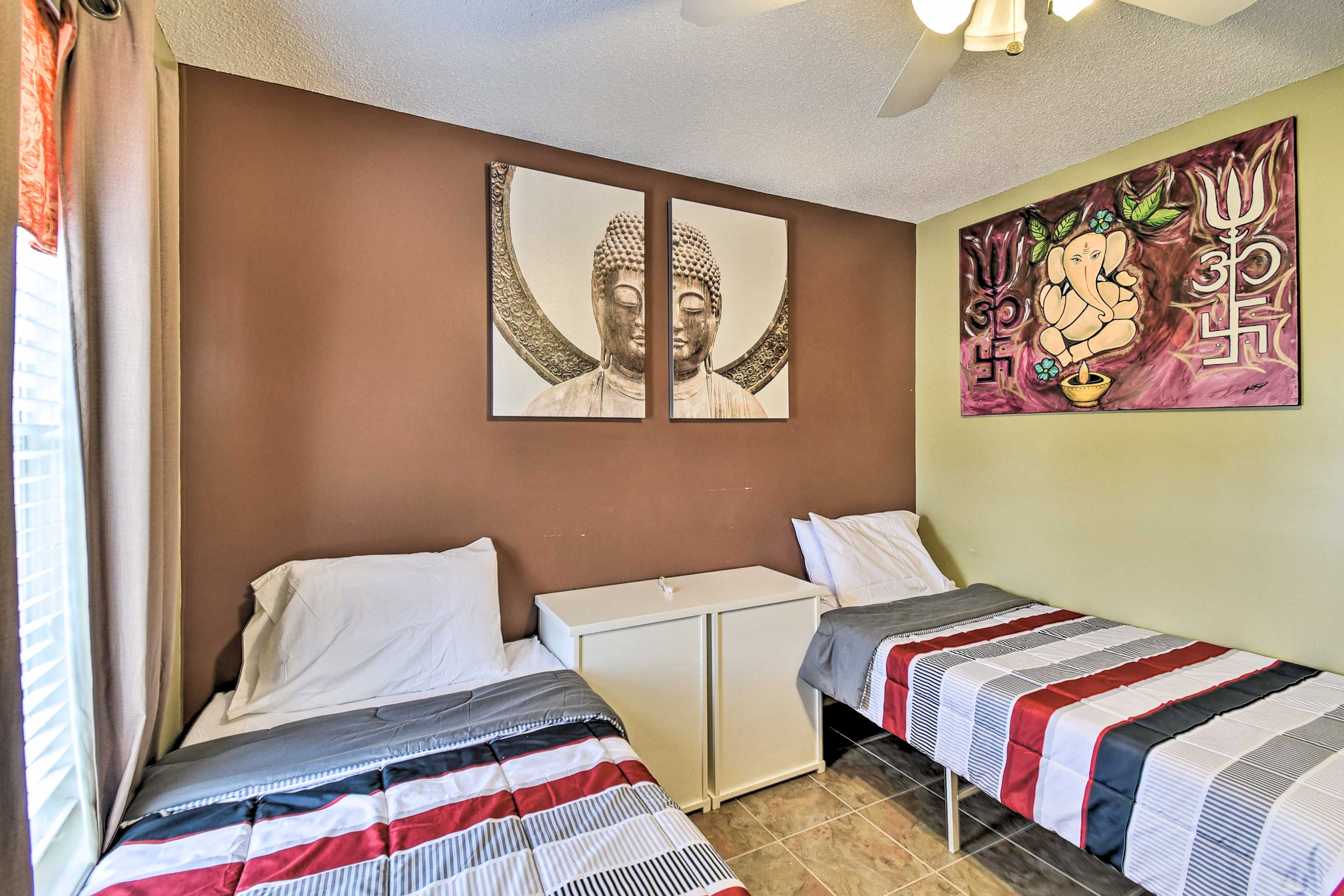 A room with two beds, a white cabinet, and a wall with religious artwork.