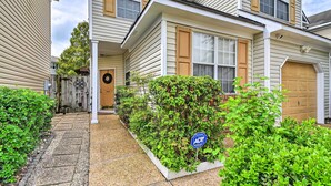 A two-story residential building with a covered front porch, a garage, and a landscaped front yard with a small garden bed. - Hampton Home w/ Fireplace + Close to Beaches! (Hampton)