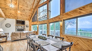 Un intérieur en bois comprenant un coin repas, une cheminée et de grandes fenêtres donnant sur une terrasse.