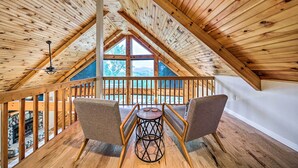 Un intérieur en bois avec un plafond haut, une table entourée de chaises et une vue dégagée grâce à de grandes fenêtres.