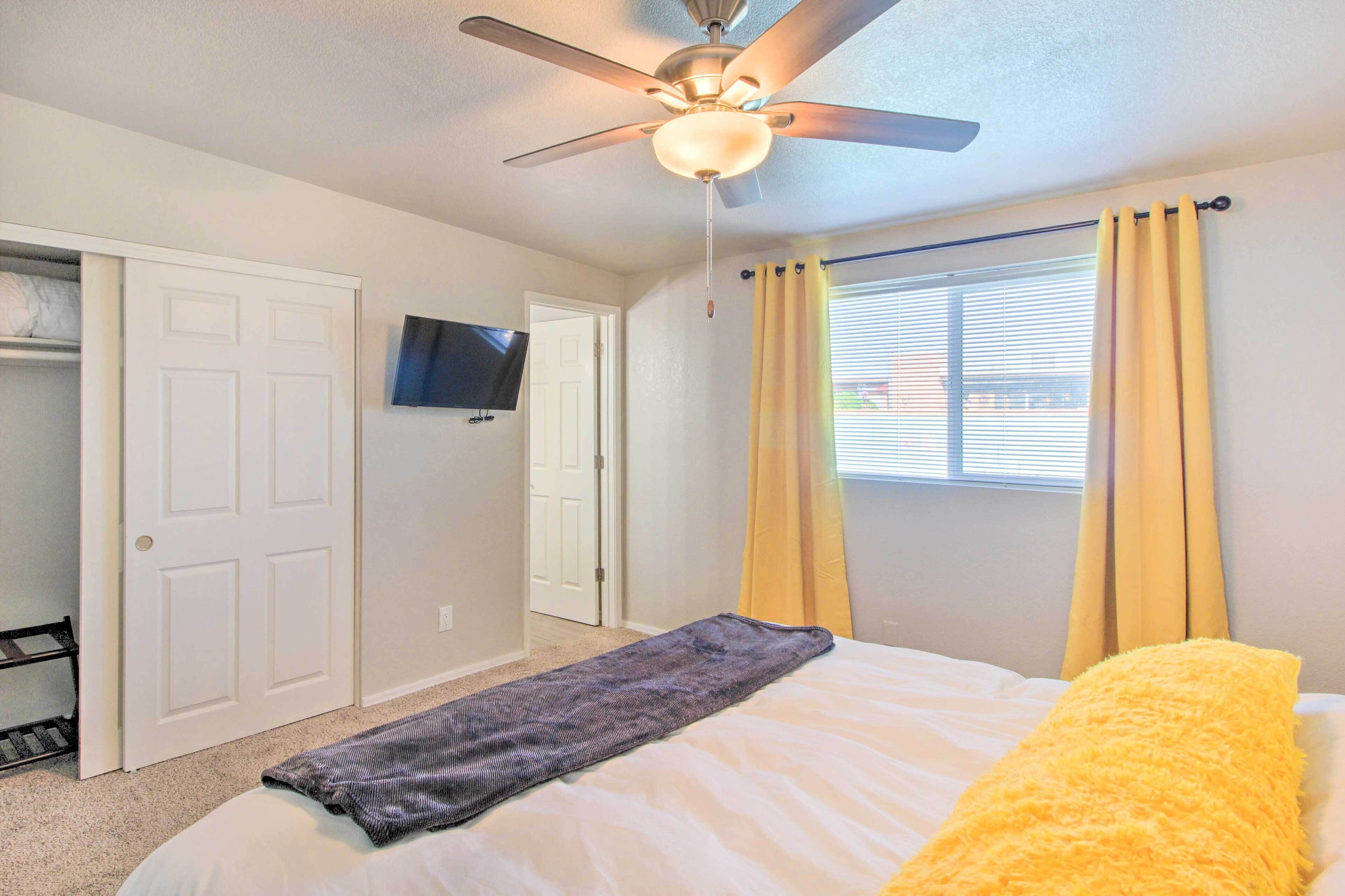 Une chambre à coucher avec un lit, un ventilateur de plafond, une fenêtre avec des rideaux et un téléviseur fixé au mur.