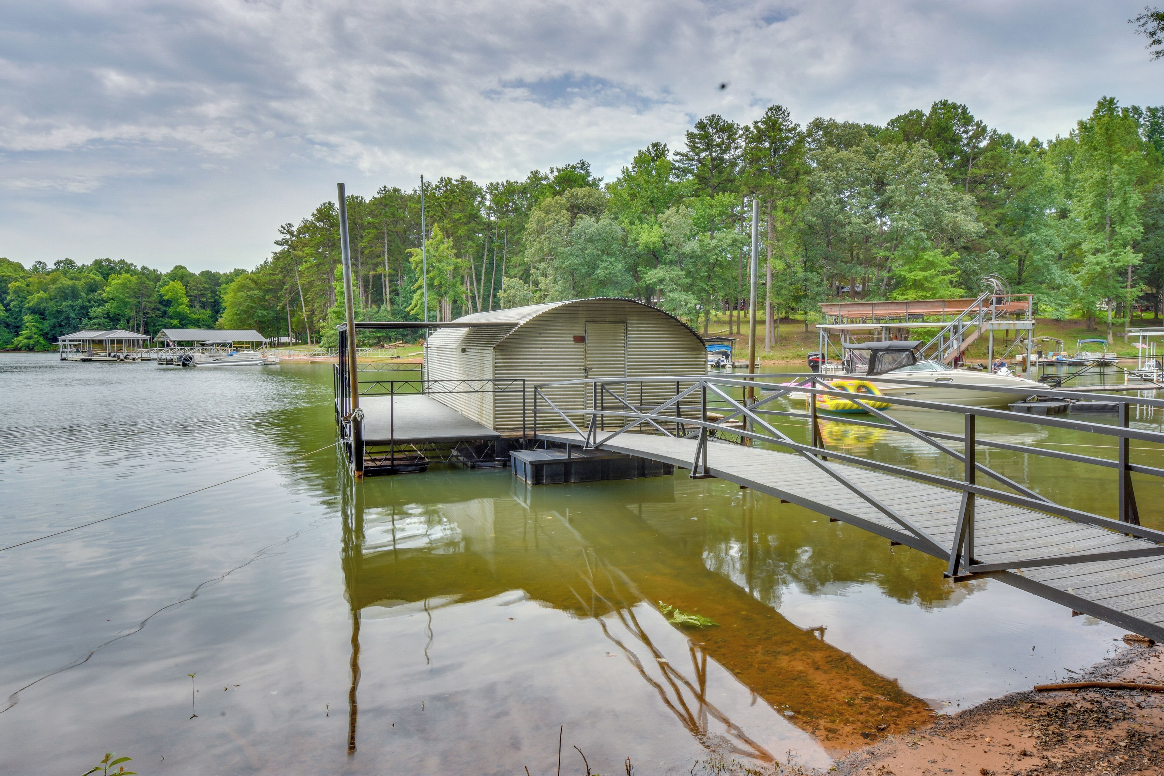 A lakeside dock with a covered boat storage area, a small bridge, and a boat ramp.