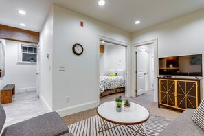 A modern living room with a sofa, a round coffee table, and a television. There is a hallway leading to a bedroom with a bed and a window. - Near Lumen Field! Walkable Dtwn Seattle Condo (Seattle)