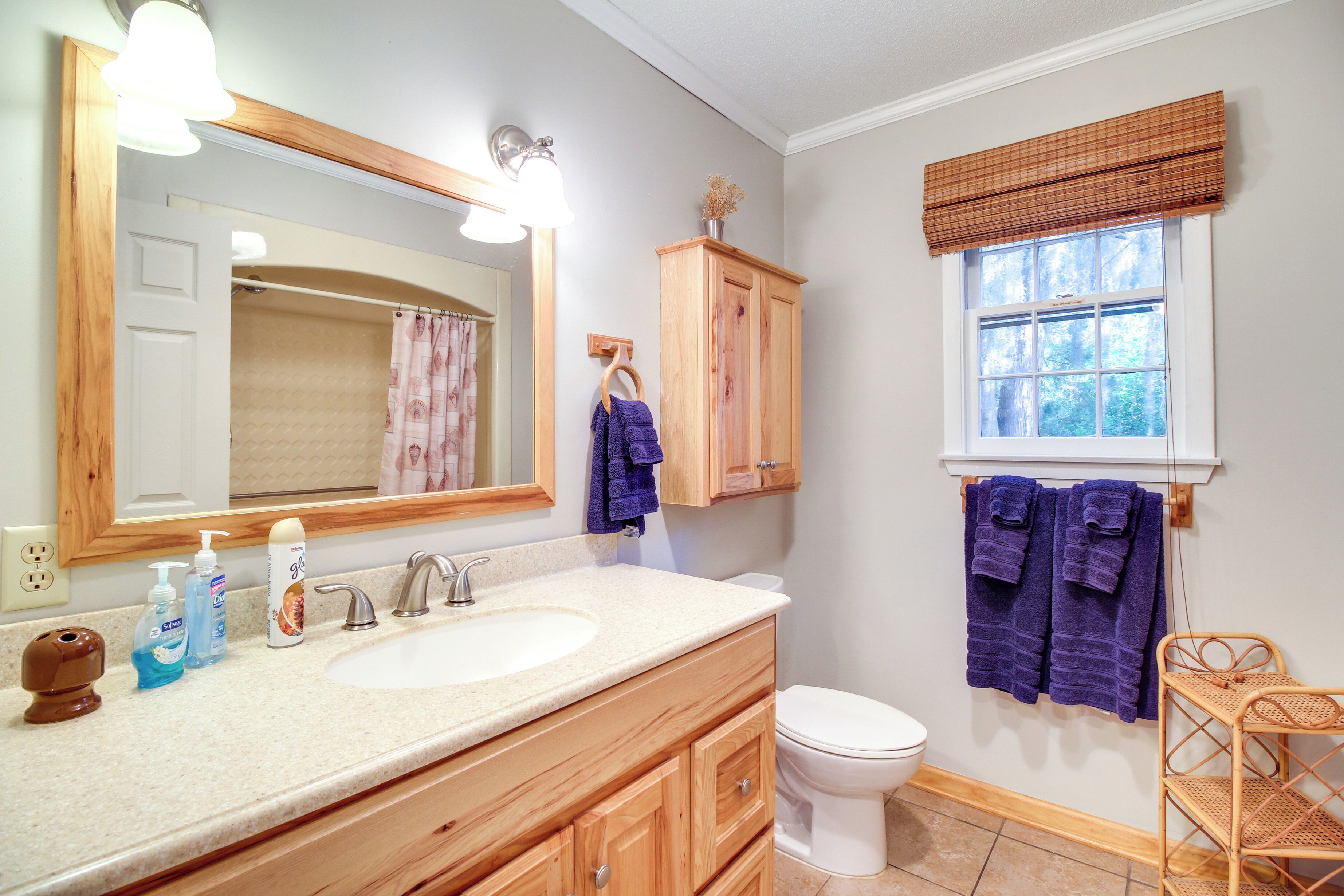 Une salle de bain avec un meuble-lavabo en bois, un évier, un miroir, des toilettes et une fenêtre donnant sur des arbres.