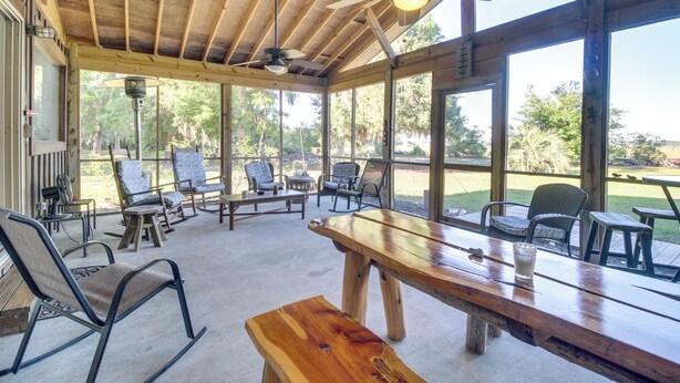 A covered outdoor seating area with wooden tables and chairs, large windows, and ceiling fans. - Dock & Views! Waterfront Baisden's Bluff Home (Crescent)