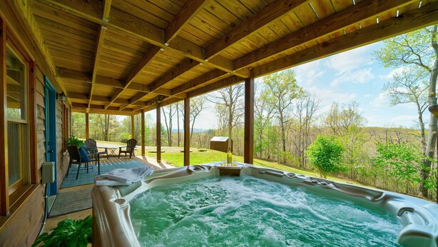 Eine Holzterrasse mit Whirlpool, Sitzgelegenheit und Blick auf die umliegenden Bäume.