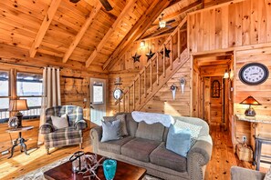 L’intérieur d’un chalet accueillant, avec un escalier en bois, un canapé, un fauteuil et une table sur laquelle se trouve une lampe.