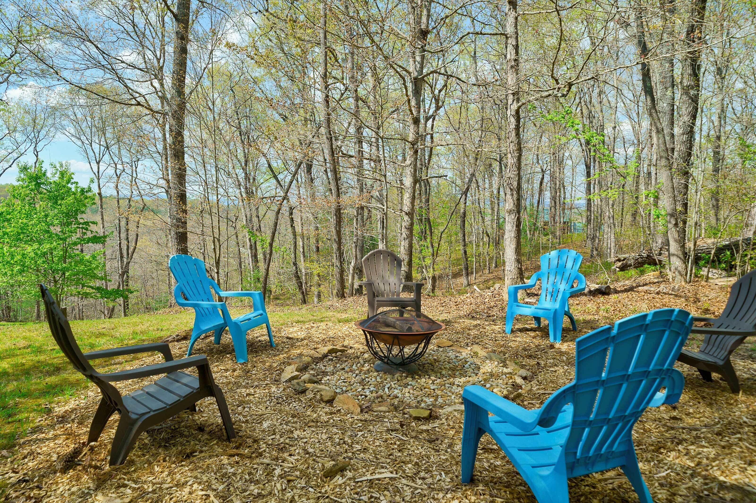 An outdoor seating area with Adirondack chairs and a central fire pit surrounded by a forest.