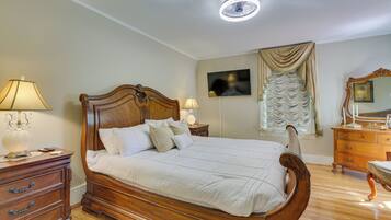 A bedroom with a wooden bed, two bedside tables, a dresser, a television, and a ceiling light.