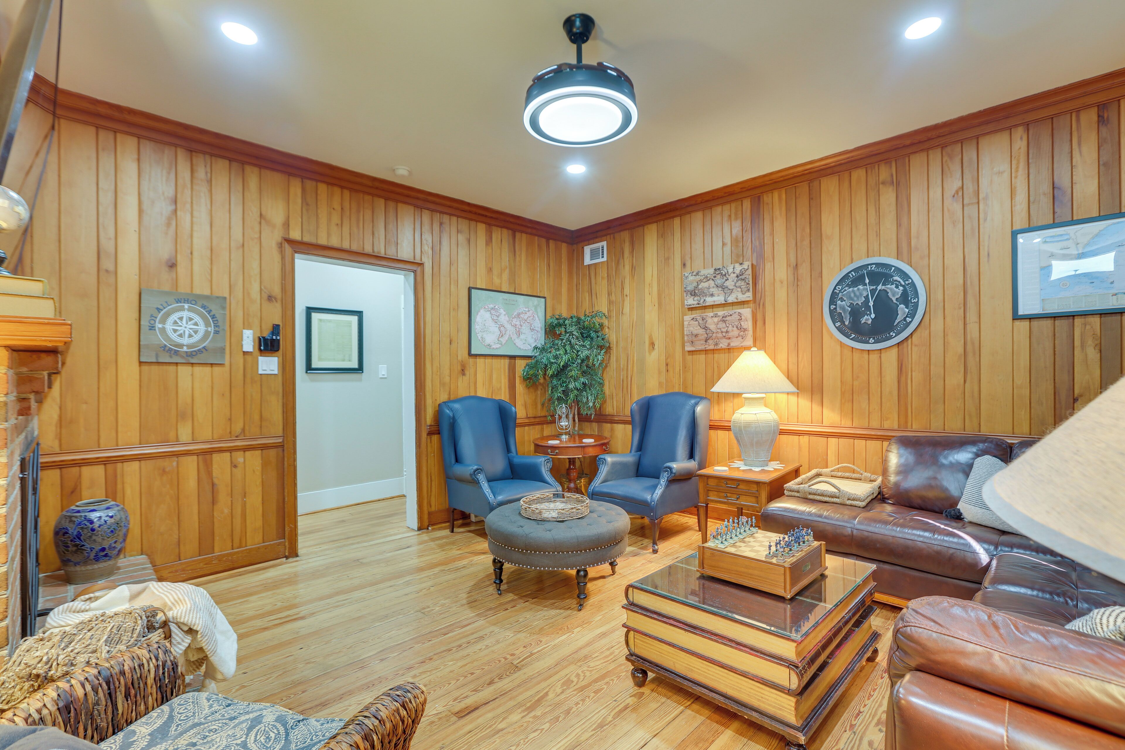 A wooden-paneled room with a leather sofa, two armchairs, a round ottoman, a lamp, and a chessboard.