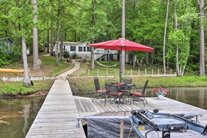 A wooden dock extending into a calm body of water, with a red umbrella and outdoor seating area. - Lakefront Sparta Home: Fire Pit, Dock & Kayak (Milledgeville)